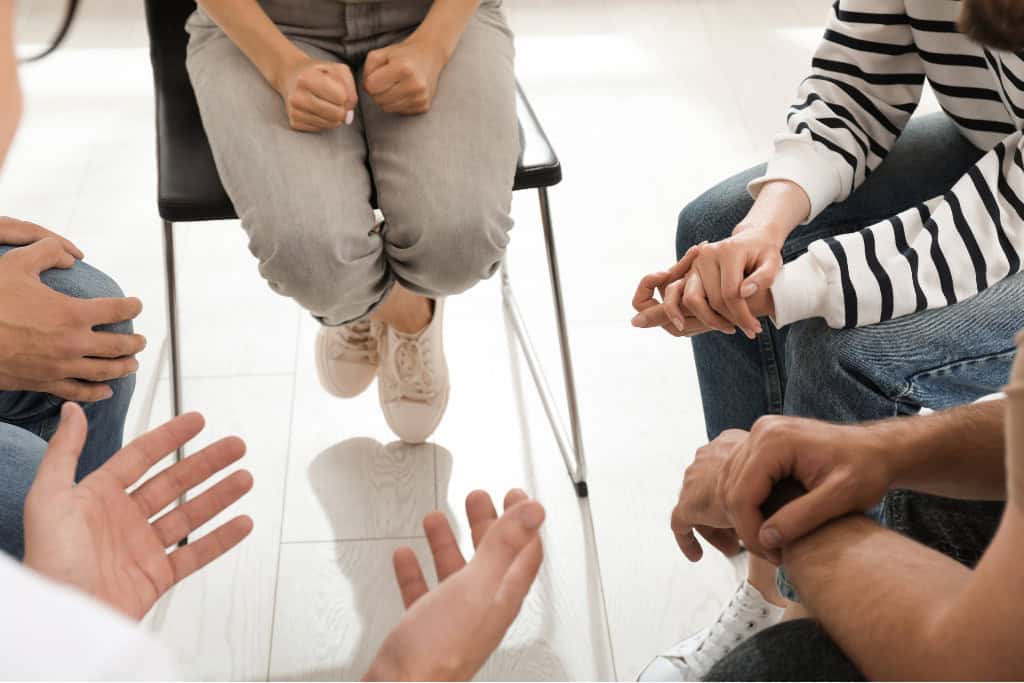 A support group session with individuals sitting in a circle, hands gesturing in conversation, highlighting a therapeutic environment for opiate addiction treatment in Reseda, CA.