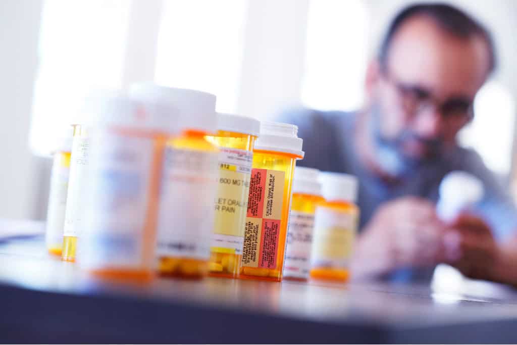 Prescription pill bottles lined up in focus with a blurred figure in the background, symbolizing the struggle with opiate addiction. This image is relevant to opiate addiction treatment in Reseda, CA.