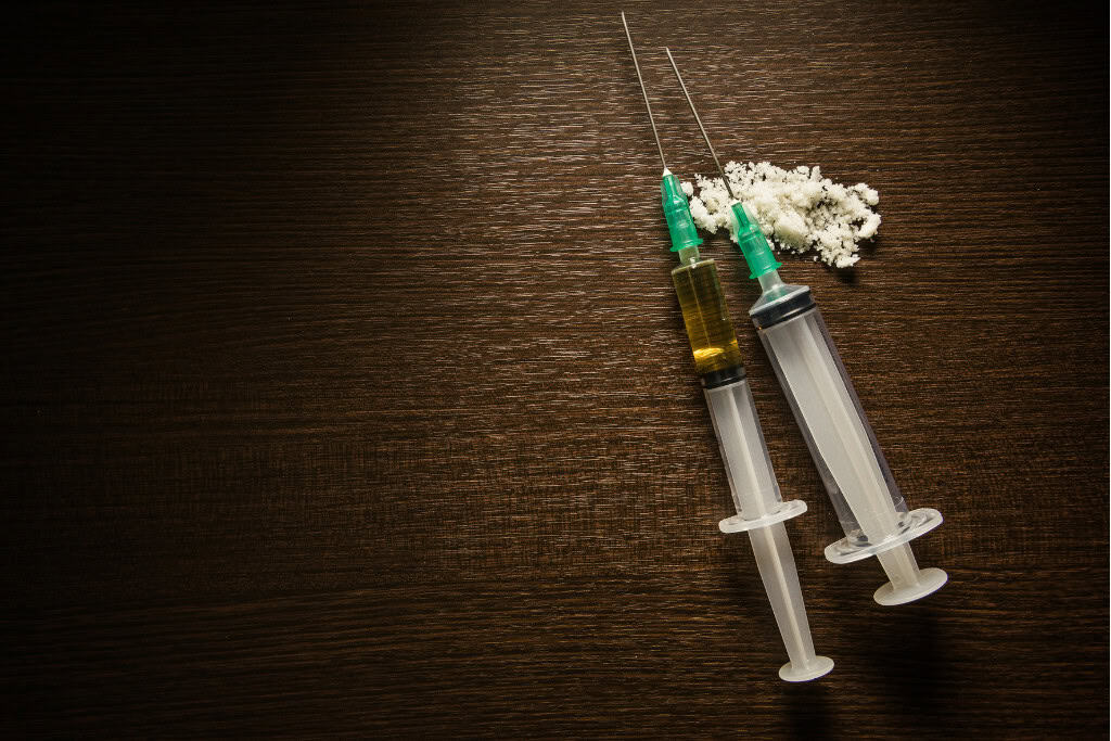 Two syringes lying on a dark wooden surface next to a pile of powdered substance, representing the seriousness of heroin addiction. This visual stresses the importance of heroin addiction treatment in Reseda CA.