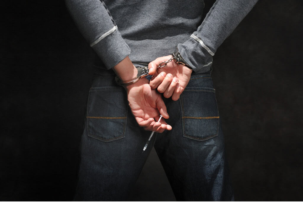 A close-up of a person with their hands behind their back in handcuffs, holding a syringe, symbolizing the struggles of heroin addiction. This image emphasizes the need for heroin addiction treatment in Reseda CA.