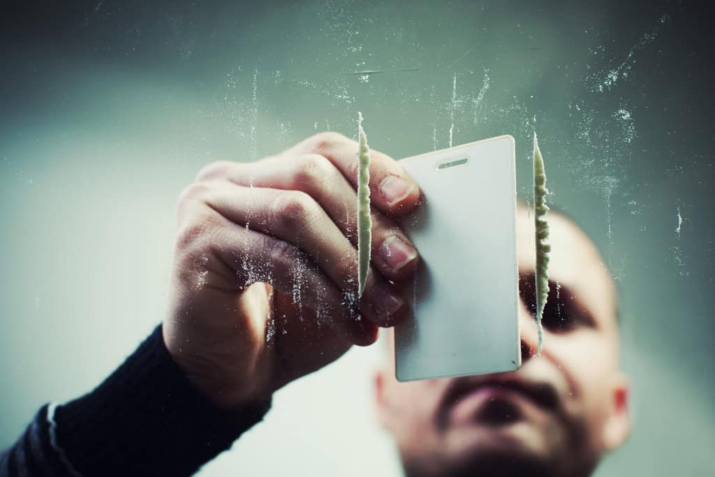 A man using a card to prepare lines of a white substance, visually capturing the challenges of substance abuse. This image connects to the services for cocaine rehab in Reseda CA.
