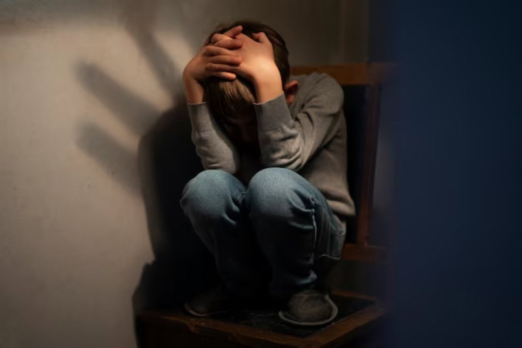 A young child huddles in a corner, covering his head, with shadows in the background suggesting fear. Trauma Therapy in Reseda, CA provides specialized support for children and adults to process and heal from traumatic events.