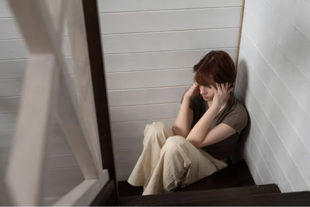 A woman sitting alone on the floor, holding her head in distress, reflecting the struggles of depression and the need for treatment options in Reseda, CA.