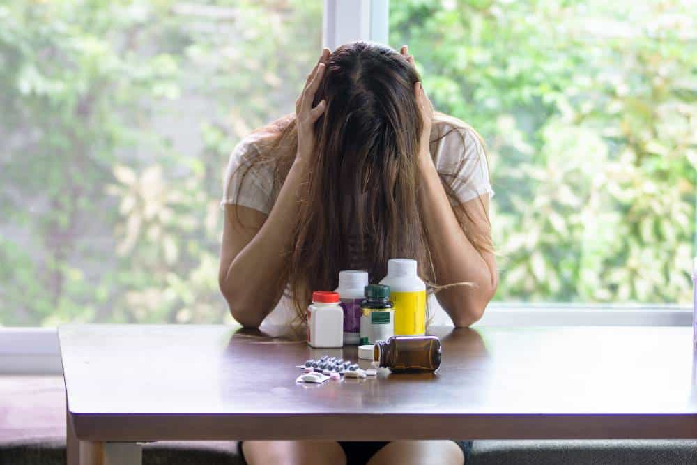 Distressed woman with head in hands near medicine bottles, illustrating Fentanyl Detox in Reseda CA.