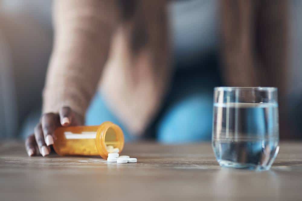 Close-up of hand reaching for spilled prescription pills and water glass during Fentanyl Detox in Reseda CA.