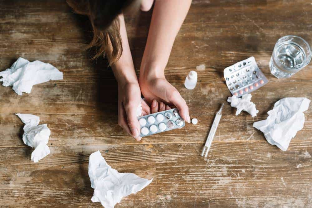Hands holding blister packs of medication on a wooden table during Opiate Detox in Reseda, CA.